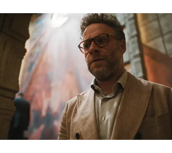 Golden Globes winner, Seth Rogen, in The Studio (2025), in a beige suit, stands in a dimly lit room, exhibiting a serious expression. A colorful, abstract wall mural behind him.