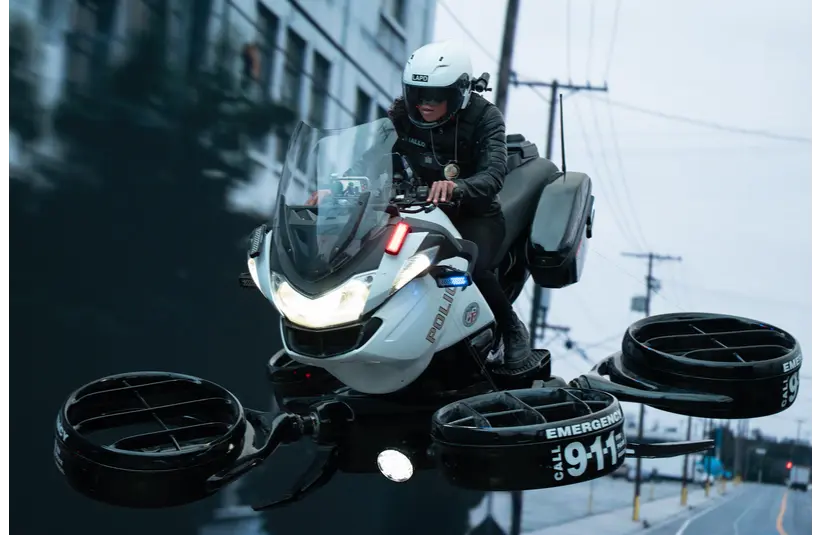 A police officer in the movie "Mercy" rides a futuristic hoverbike in an urban setting. The sleek white vehicle hovers above the street, conveying speed and innovation.