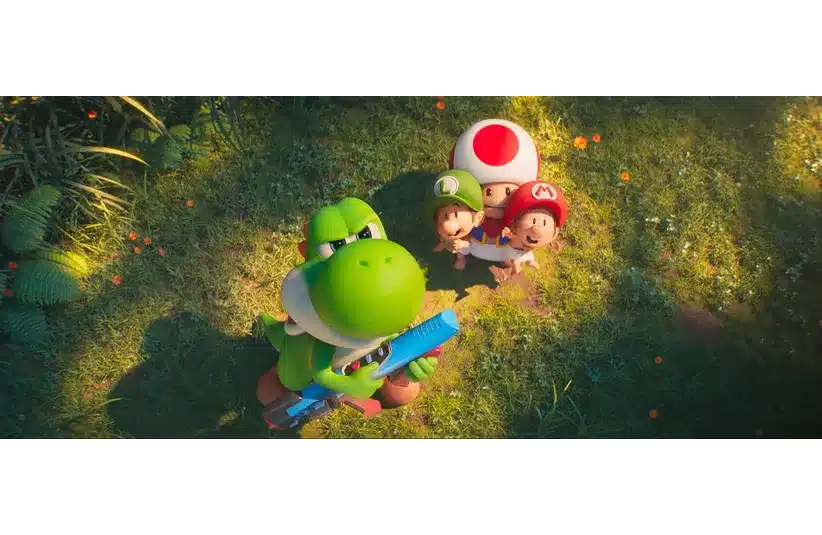 Yoshi, a green dinosaur-like character with a blue weapon, stands in a sunlit grassy field, surrounded by three small, colorful companions looking upwards. Playful and adventurous mood in "The Super Mario Bros. Galaxy Movie."