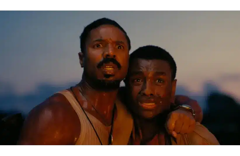 Michael B. Jordan and Miles Caton in Sinners (2025), visibly distressed, stand close together at dusk. One has his arm around the other, and both appear sweaty and intensely focused ahead.