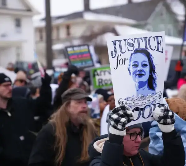 A diverse group of protesters holds signs, including one reading "Justice for Good," in a winter setting. The mood is determined and focused. Showing support in Minneapolis for Renee Nicole Good's death and leading towards her GoFundMe fundraiser.