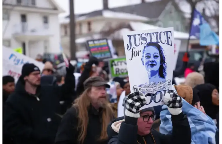 A diverse group of protesters holds signs, including one reading "Justice for Good," in a winter setting. The mood is determined and focused. Showing support in Minneapolis for Renee Nicole Good's death and leading towards her GoFundMe fundraiser.