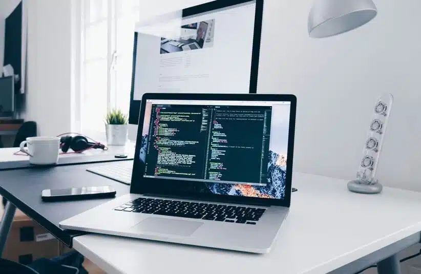 A sleek laptop with a blank screen sits on a wooden desk. To the left are gold geometric bookends, and to the right is a small potted plant, creating a minimalist and tidy workspace.