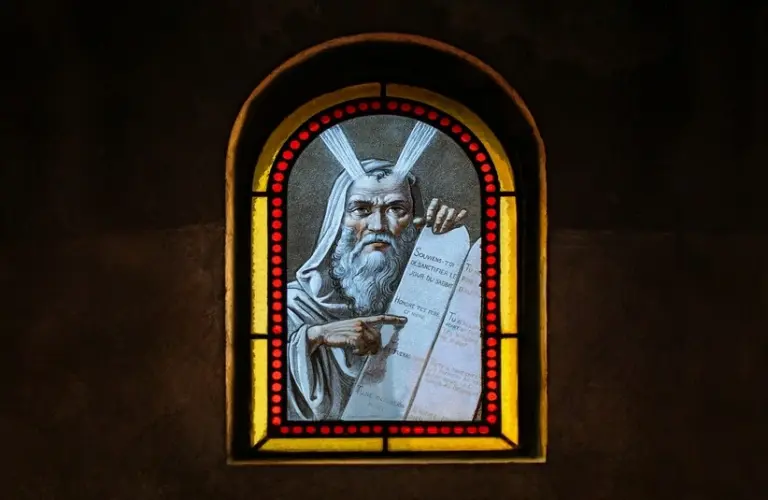 Stained glass, moses from the book of Exodus, paint-on-glass window, inside a cemetery sepulcher (a small, upright stone chapel above a burial plot). Moses is the subject of Exodus.