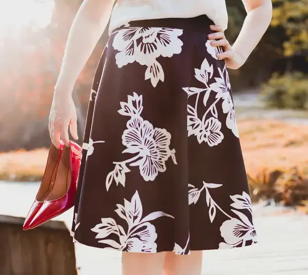 A person wearing a floral skirt holds red high heels represents spring fashion trends.