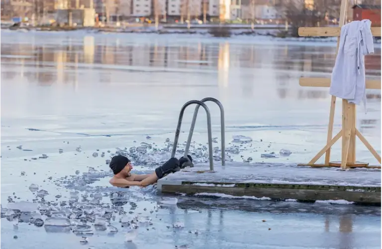 A man wearing a hat and gloves swims in an icy lake following cold plunging trend