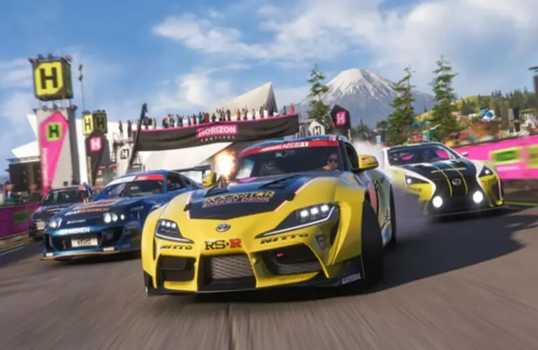 Three race cars speed around a track in Forza Horizon 6, led by a yellow car, with a mountain and cheering crowd in the background. Energetic and competitive vibe.