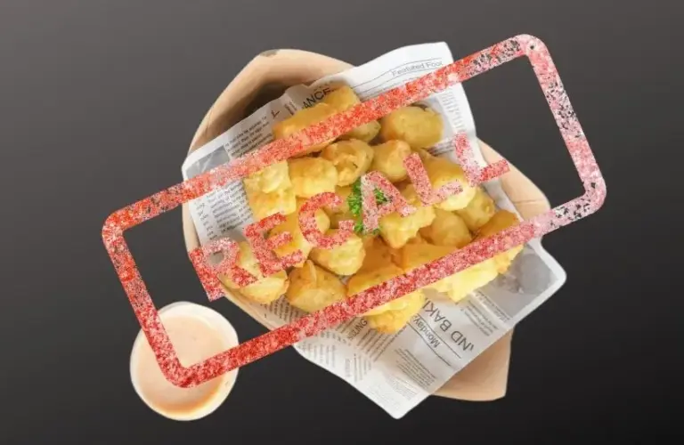 Golden tater tots on newspaper with parsley garnish, placed on a paper tray. A small cup of light brown dipping sauce is beside it with Recall stamped over it.