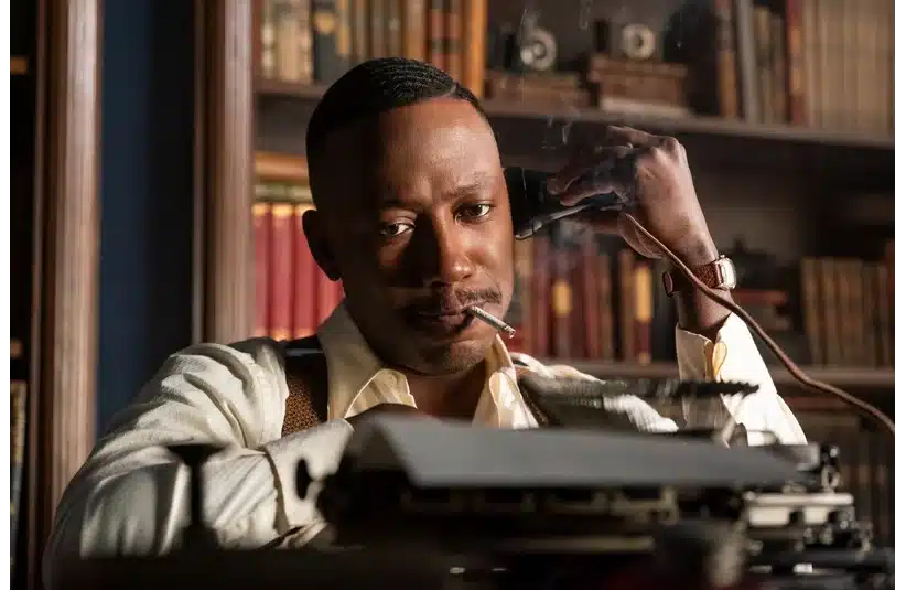 A man in a vintage suit leans back, talking on a rotary phone with a cigarette in his mouth, in a cozy library setting lined with books.