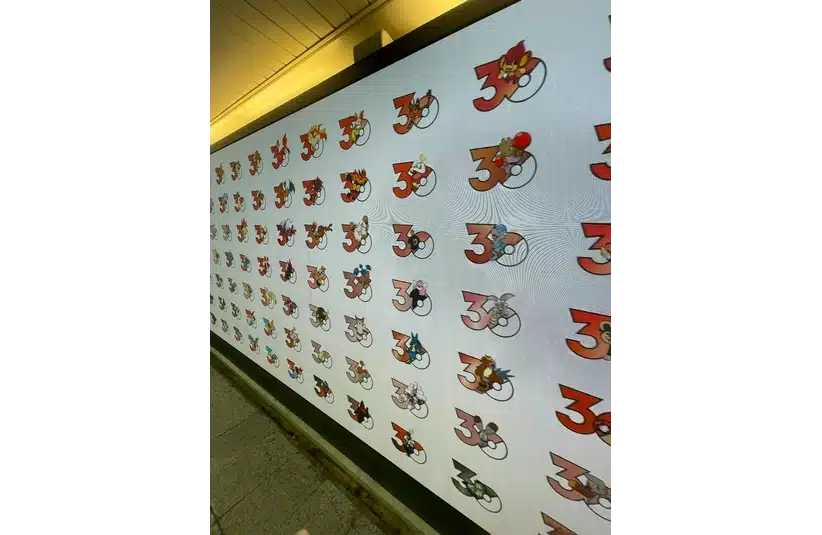 A brightly lit wall display with Pokemon inside the number "30" repeated in a grid pattern. The scene is lively and playful.