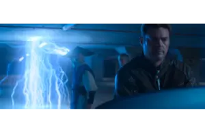 Three people, in Mortal Kombat 2, stand in a dimly lit room. Blue lightning arcs from the ceiling. The mood is tense, with focus on a man in a leather jacket in the foreground.