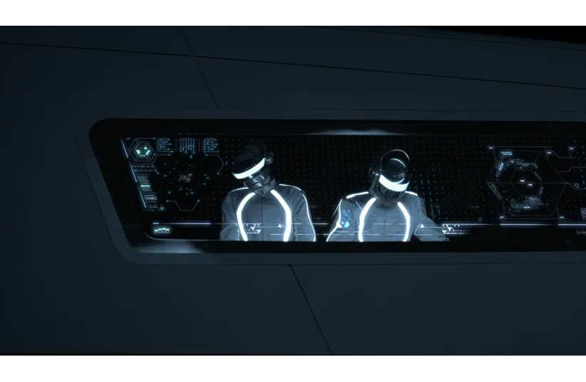 Two individuals, Daft Punk, in futuristic attire with glowing lines sit at a high-tech control panel, wearing visors. The atmosphere is sleek and technological.