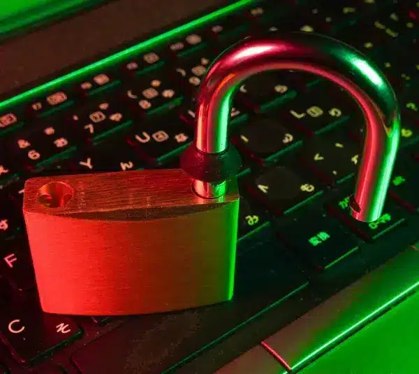 Discord is working on age verification. A glowing red and green light illuminates an open padlock resting on a laptop keyboard, symbolizing cyber security vulnerability or data breach.