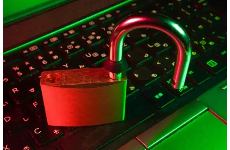 Discord is working on age verification. A glowing red and green light illuminates an open padlock resting on a laptop keyboard, symbolizing cyber security vulnerability or data breach.