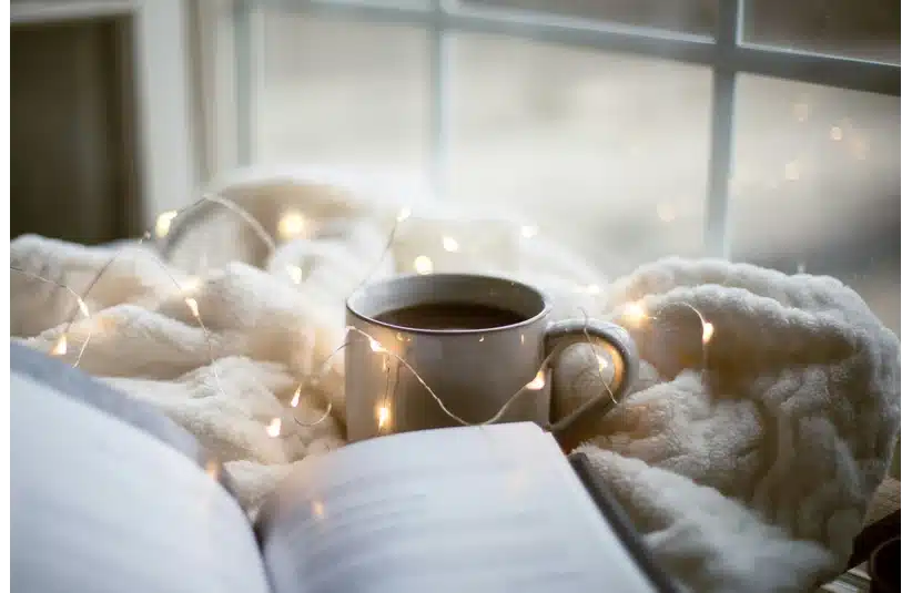 a cozy setting with a book, soft blanket, fairy lights, and a warm cup of coffee