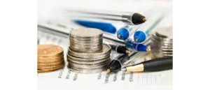 Stacks of silver and gold coins, a cluster of ballpoint pens, financial documents depicting financial realism and business planning