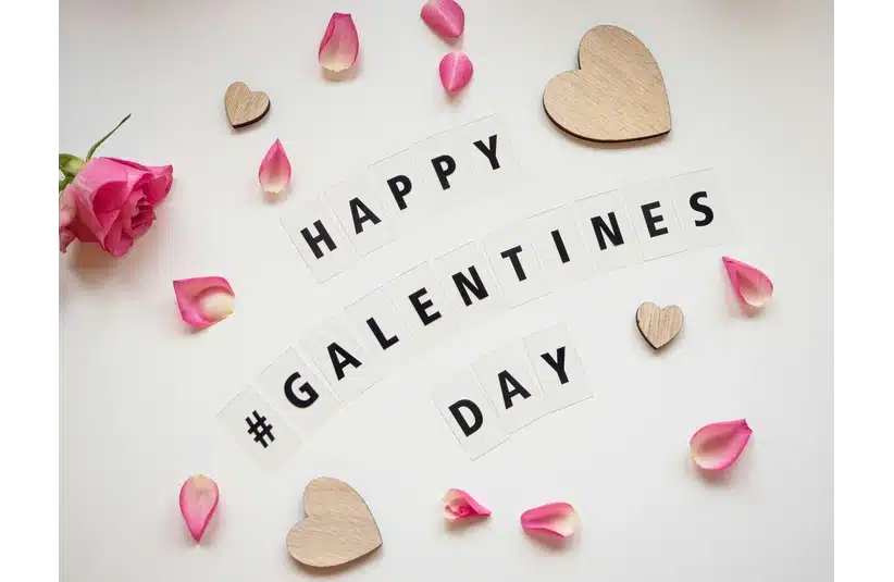 "Galentine's Day message on white background with pink rose, scattered petals, and wooden hearts. Festive, cheerful, and friendship-focused theme."