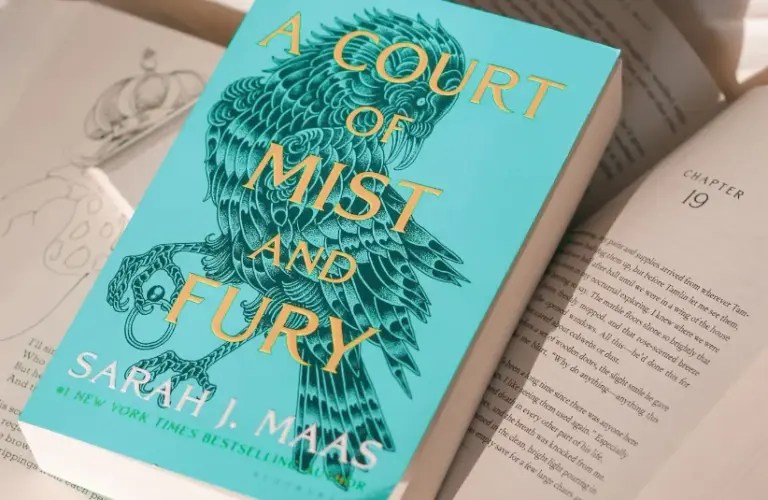 A copy of Sarah J. Maas' "A Court of Mist and Fury" lying on a pile of open books