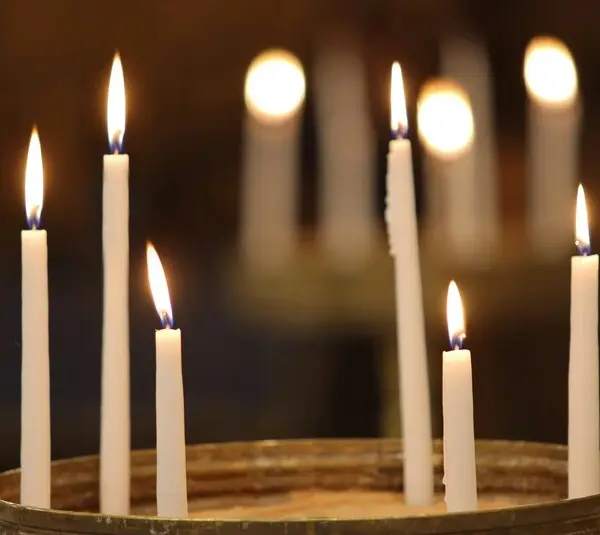 Seven lit white candles in sand create a serene and warm ambiance against a blurred dark background, evoking feelings of peace and reflection. Holy Thursday. Maundy Thursday
