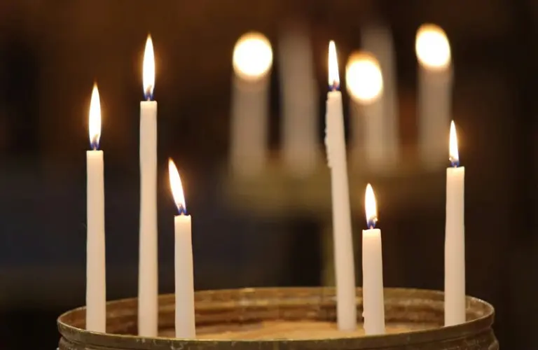 Seven lit white candles in sand create a serene and warm ambiance against a blurred dark background, evoking feelings of peace and reflection. Holy Thursday. Maundy Thursday