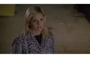 Sarah Michelle Gellar as Buffy Summers in "Buffy the Vampire Slayer" looks up with a serious expression, wearing a black and white leopard print jacket. The background is dimly lit and neutral.