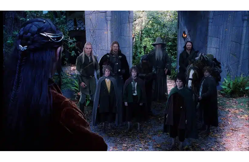 A group of nine characters stands solemnly facing an elf with long dark hair in a wooded, stone archway setting. They appear determined and united. Lord of the Rings