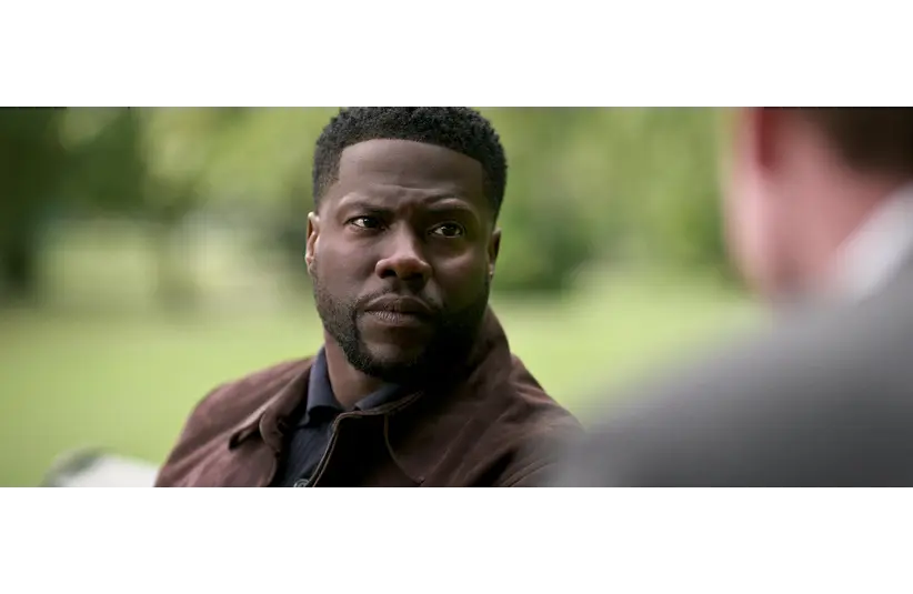 Image of Kevin Hart looking solemnly at someone, who is maybe having a conversation with him.  He has a dark brown jacket on with a black button down underneath.