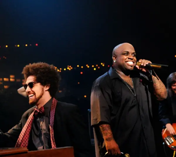 Gnarls Barkley performs on stage, featuring Danger Mouse with sunglasses playing keyboard and Cee-Lo Green singing with a microphone. The background is adorned with colorful lights.