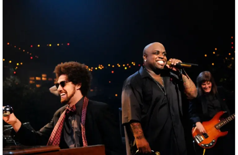 Gnarls Barkley performs on stage, featuring Danger Mouse with sunglasses playing keyboard and Cee-Lo Green singing with a microphone. The background is adorned with colorful lights.