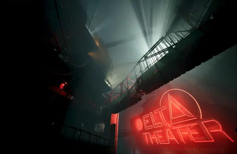 Dimly lit industrial space in Sleep Awake with overhead walkways and beams of light piercing through. A neon sign reads "Delta Theater," creating a mysterious, immersive atmosphere.