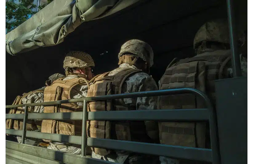 Soldiers wearing helmets and camouflage uniforms sit in a dimly lit military truck, conveying a sense of readiness and focus.