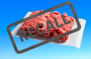 Ground beef on paper against a blue background, overlaid with a bold "RECALL" stamp, indicating a product recall alert.