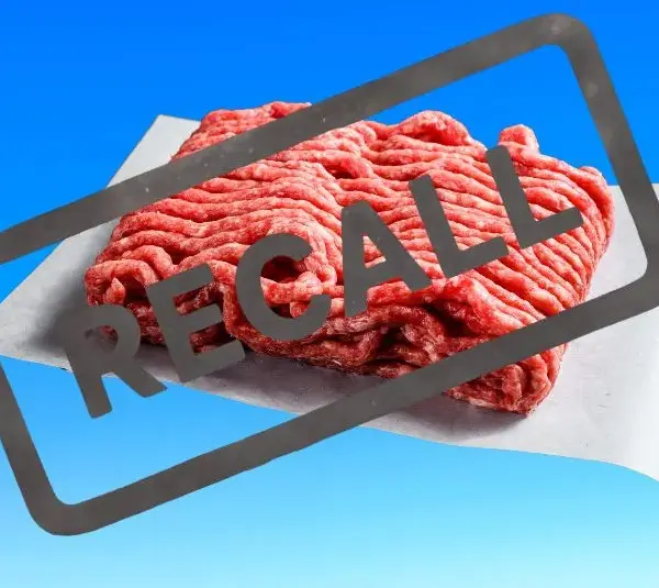 Ground beef on paper against a blue background, overlaid with a bold "RECALL" stamp, indicating a product recall alert.