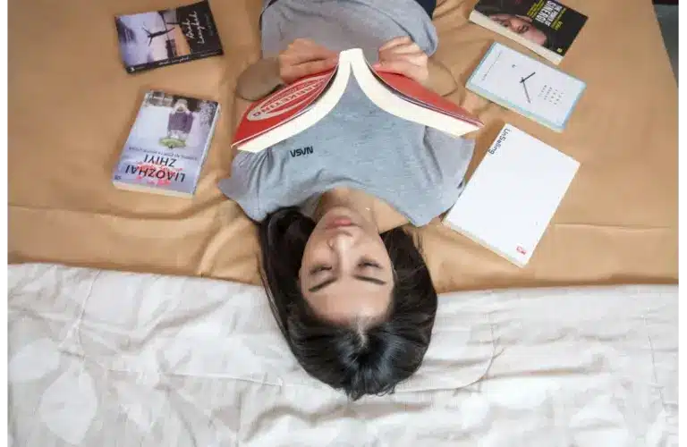 A woman laying down with books laid out on a bed, reading.