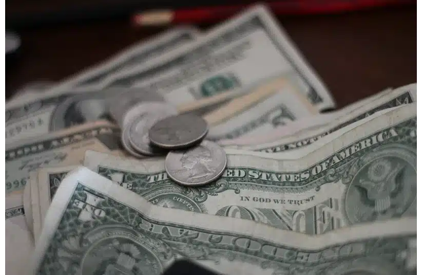 Close-up of assorted U.S. dollar bills and coins scattered on a surface. The focus is on a one-dollar bill with a few quarters on top.