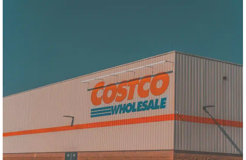 A Costco Wholesale store facade with large, bold orange and blue signage against a clear blue sky, conveying a calm, spacious ambiance.