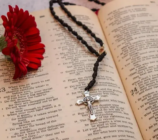 In daily devotion, an open Bible is shown with a rose and cross necklace inside.