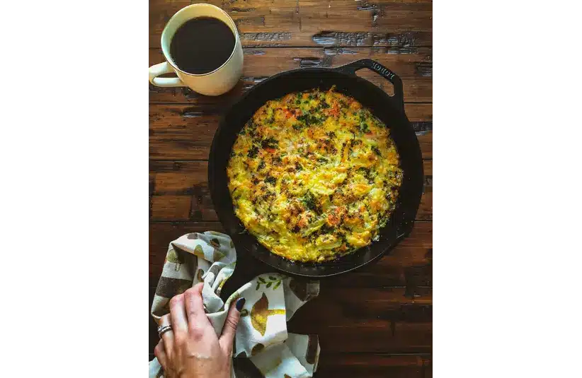 A fresh spring veggie frittata in a cast iron pan with a cup of black coffee on the side
