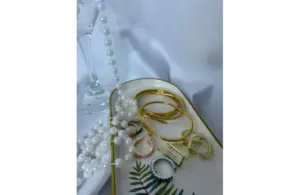 A tray with several gold and silver bangles, rings, and a string of white pearls on a white surface showing metallic accessories for everyday chic