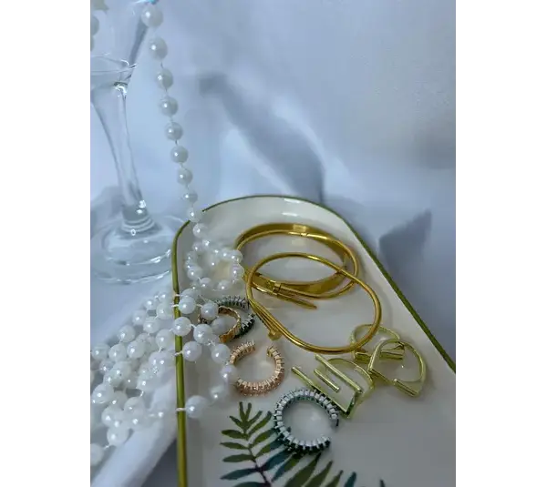 A tray with several gold and silver bangles, rings, and a string of white pearls on a white surface showing metallic accessories for everyday chic