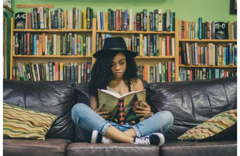 A woman reading a book with a vast bookshelf in the background