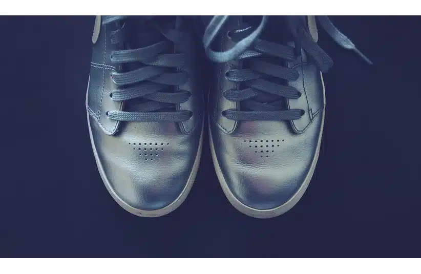 A pair of metallic silver sneakers with black laces, viewed from above, shines against a dark background.