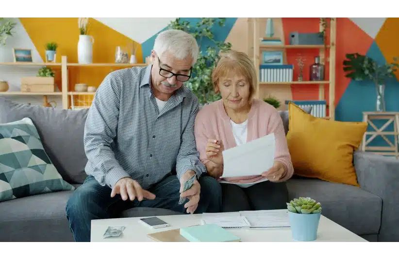A happy elderly couple are sorting bills, reviewing documents, and counting money. A photo illustrating the concept of people and financial wellness.