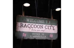 A weathered green sign lit by small lamps reads "Welcome to Raccoon City, Enjoy your stay!" and "Home of Umbrella." A foreboding nighttime forest background sets an eerie tone in Resident Evil.