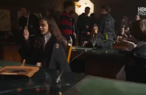Students in robes practice magic at desks with wands in a dimly lit classroom. The atmosphere is lively and focused, suggesting a magical lesson.