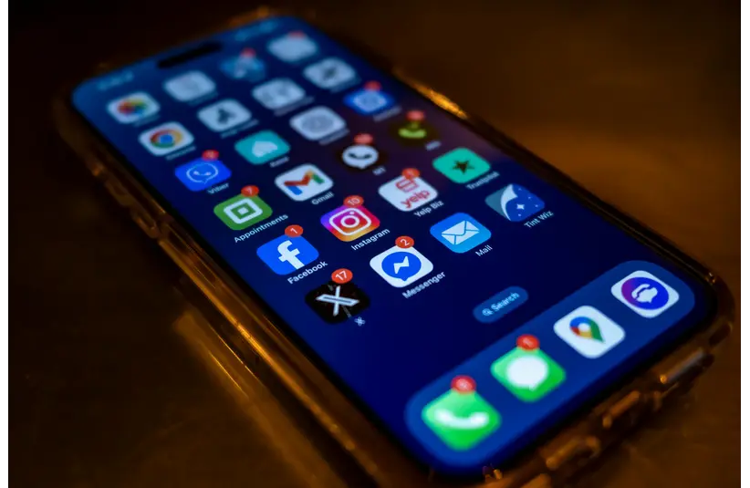 Smartphone screen showing numerous app icons with notification badges, including social media and messaging apps. The scene conveys a sense of digital busyness.
