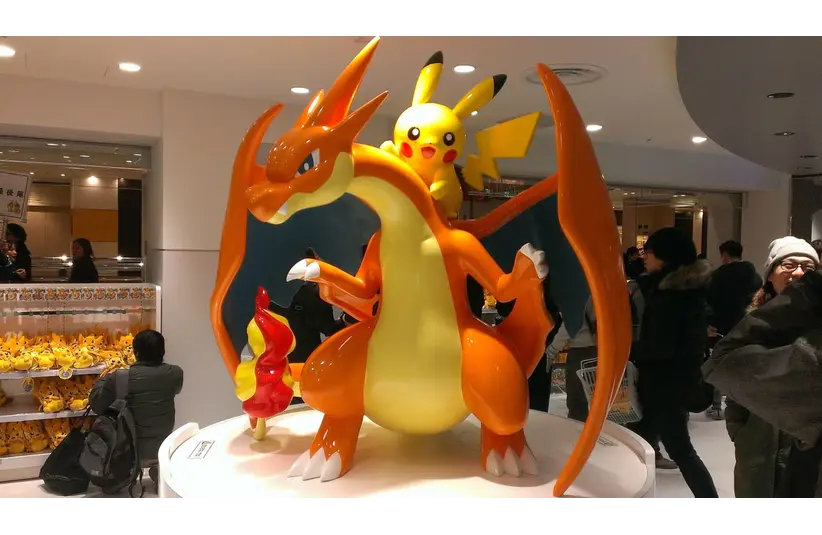 Sculpture of Charizard with Pikachu on its back inside a Pokémon Center, surrounded by visitors and shelves with Pikachu plush toys, creating a lively atmosphere.