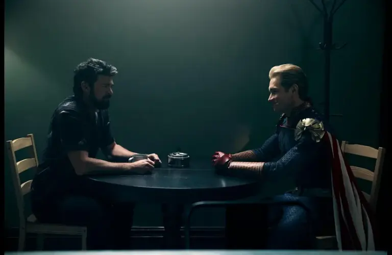 Karl Urban (Billy Butcher) and Antony Starr (Homelander) in The Boys sit across from each other at a small table in a dimly lit room, one in casual attire, the other in superhero costume, creating a tense atmosphere.