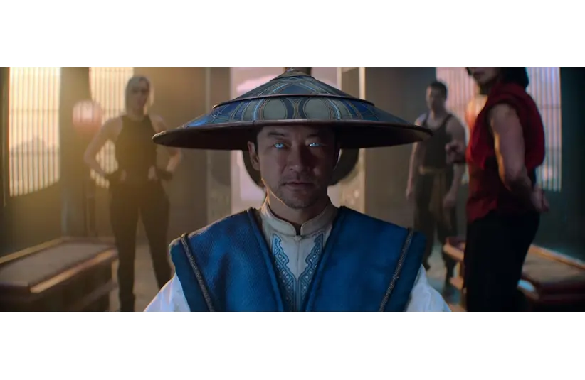 Tadanobu Asano in Mortal Kombat 2 (2026), in a blue robe and wide-brimmed hat, stares intently, his eyes glowing blue. Three people stand behind him in a dimly lit room, creating a tense atmosphere.
