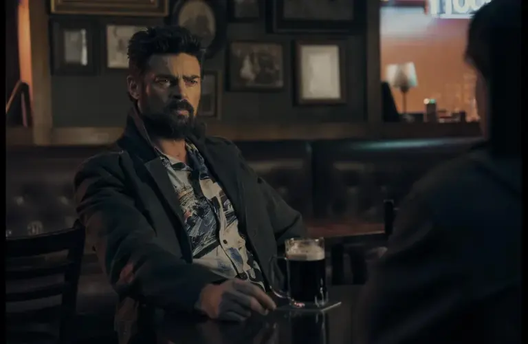 Karl Urban as Billy Butcher in The Boys, sitting in a dimly lit pub holding a mug of beer